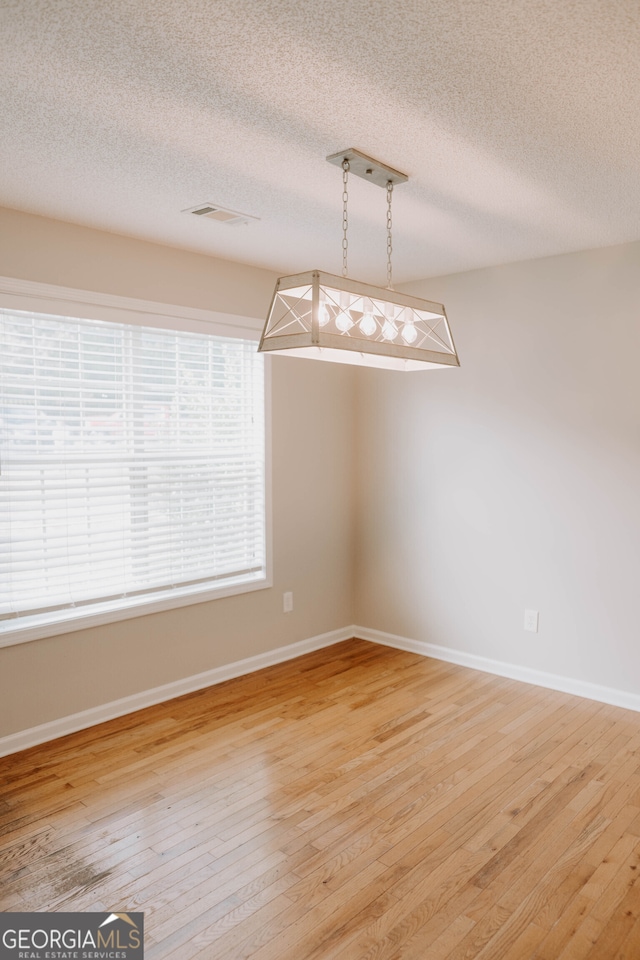 unfurnished dining area featuring wood-type flooring and a textured ceiling