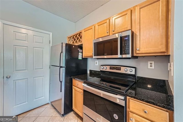 kitchen with stainless steel appliances, light tile patterned flooring, dark stone counters, and a textured ceiling