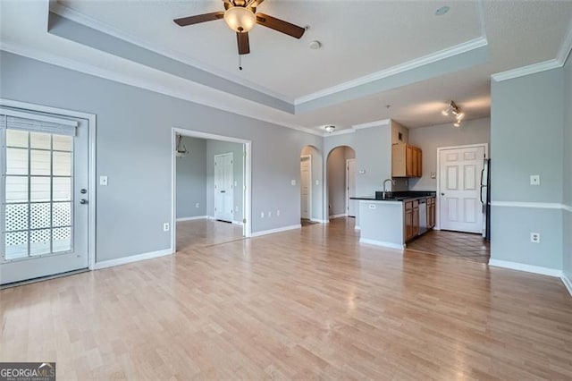 unfurnished living room with crown molding, a raised ceiling, sink, ceiling fan, and light hardwood / wood-style flooring