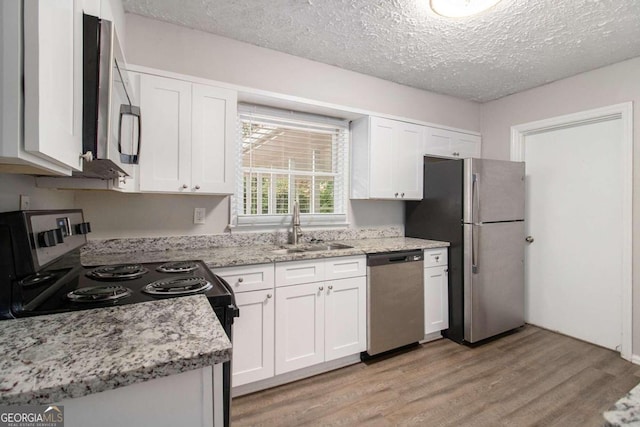 kitchen with sink, appliances with stainless steel finishes, a textured ceiling, white cabinets, and light wood-type flooring