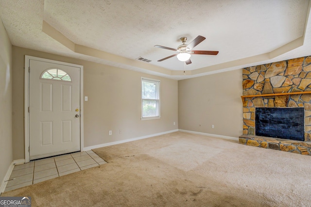 carpeted foyer featuring a tray ceiling, ceiling fan, a fireplace, and a textured ceiling