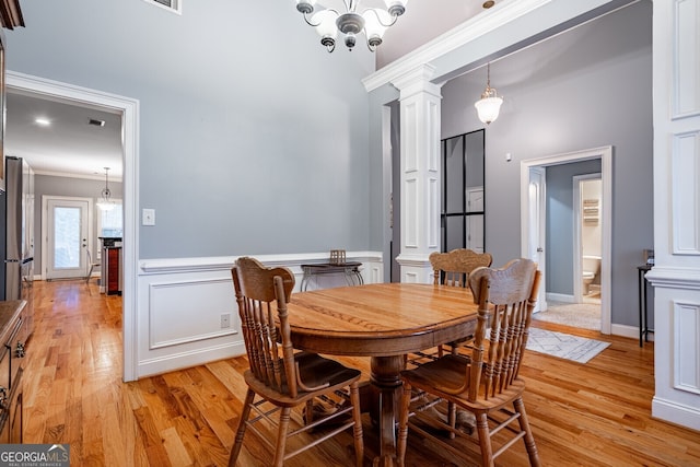 dining room with light hardwood / wood-style floors, ornate columns, ornamental molding, and a chandelier