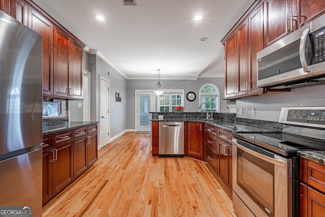 kitchen with dark stone counters, ornamental molding, stainless steel appliances, decorative light fixtures, and light hardwood / wood-style floors