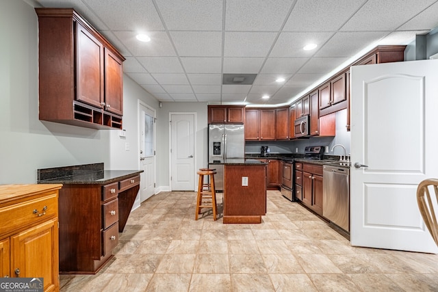 kitchen with a paneled ceiling, a center island, a kitchen bar, and appliances with stainless steel finishes