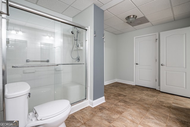 bathroom featuring a drop ceiling, toilet, and a shower with shower door