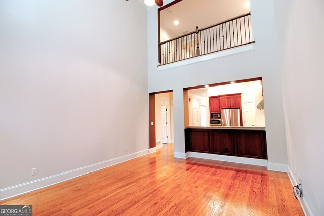 unfurnished living room featuring a high ceiling, light wood-type flooring, and ceiling fan