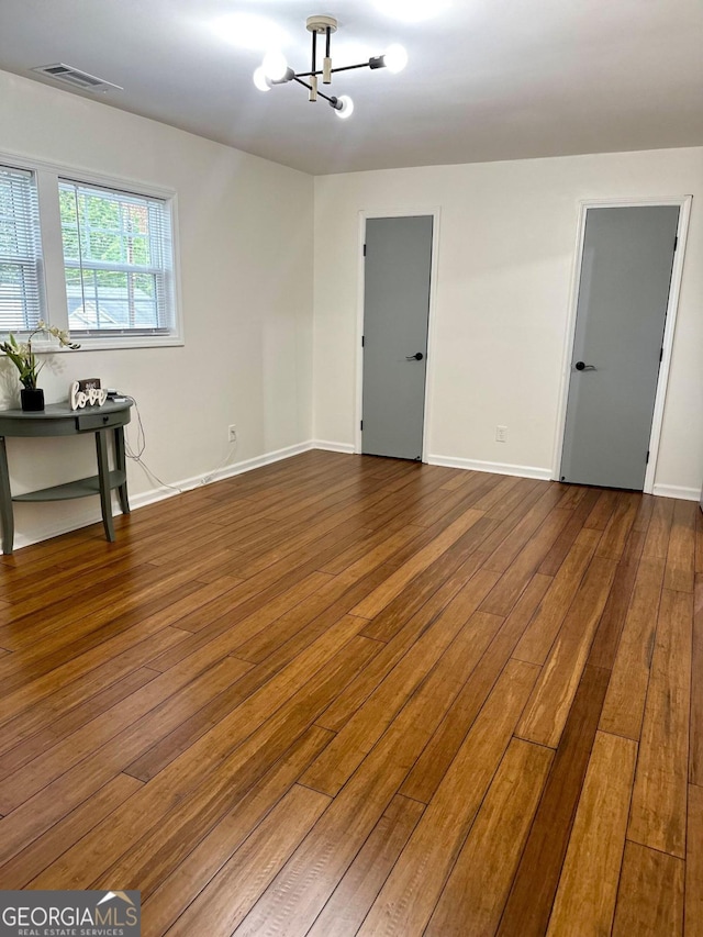 spare room featuring dark wood-style floors, a chandelier, visible vents, and baseboards