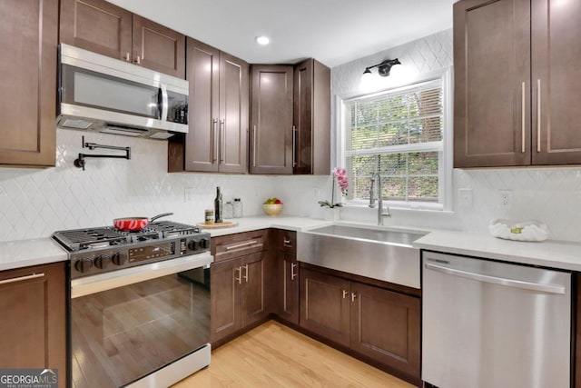 kitchen with light wood finished floors, stainless steel appliances, a sink, and light countertops