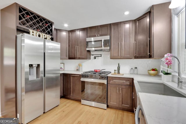 kitchen with appliances with stainless steel finishes, light stone counters, light wood-style floors, a sink, and recessed lighting