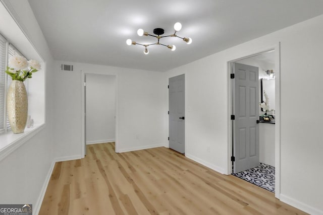 unfurnished bedroom with light wood-style floors, a walk in closet, visible vents, and baseboards