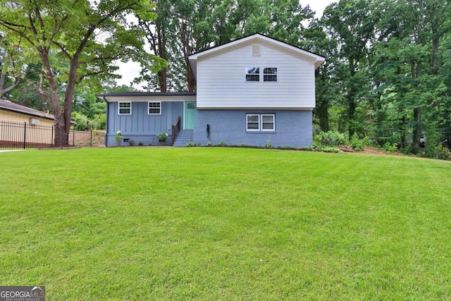 back of house featuring entry steps, brick siding, fence, a lawn, and board and batten siding