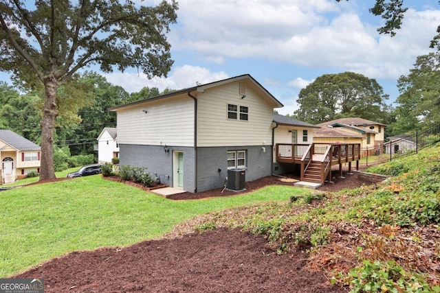 rear view of property with cooling unit, brick siding, fence, a lawn, and a wooden deck