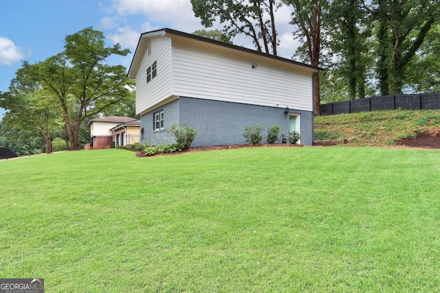 view of side of home featuring brick siding, a yard, and fence