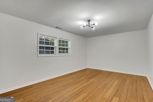 unfurnished room with light wood-style flooring, an inviting chandelier, visible vents, and baseboards