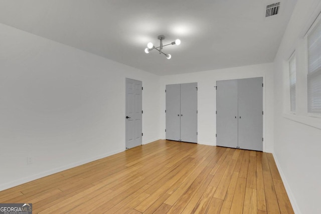 unfurnished bedroom with baseboards, light wood finished floors, visible vents, and multiple closets