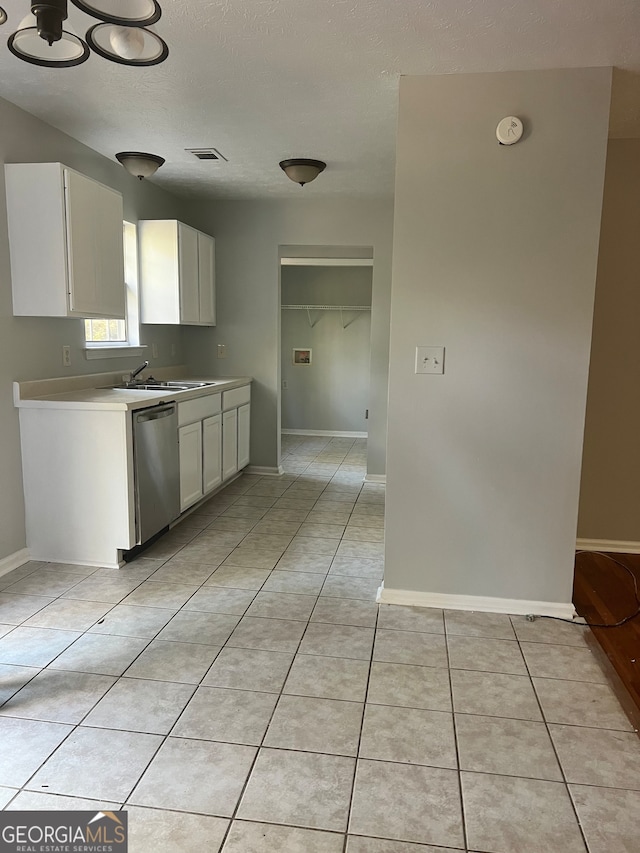 kitchen featuring sink, a textured ceiling, light tile patterned floors, stainless steel dishwasher, and white cabinets