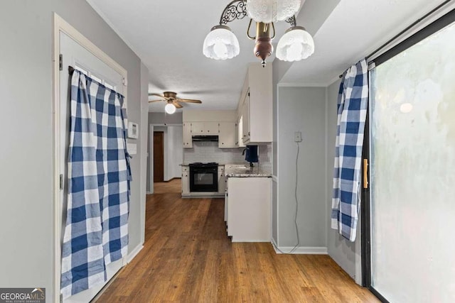 kitchen with hardwood / wood-style flooring, tasteful backsplash, decorative light fixtures, white cabinets, and black range