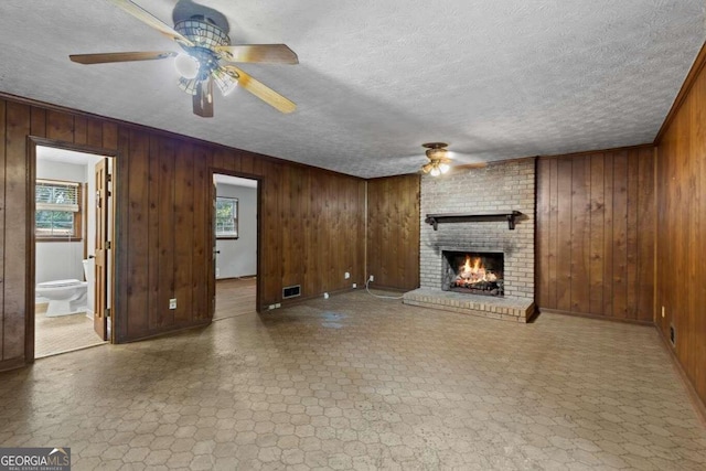 unfurnished living room featuring a brick fireplace, wooden walls, a healthy amount of sunlight, and ceiling fan