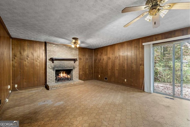 unfurnished living room with wooden walls, a textured ceiling, ceiling fan, and a fireplace