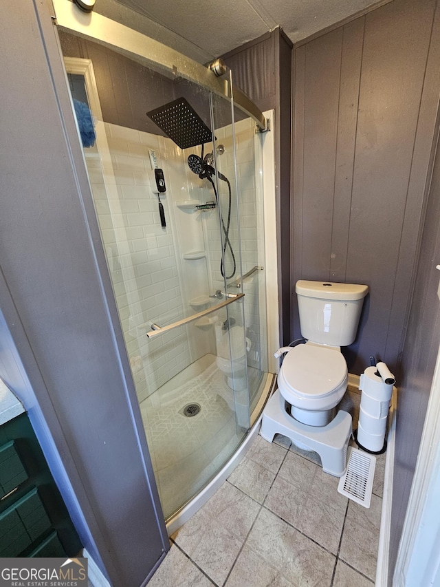 bathroom with tile patterned floors, wooden walls, a shower with shower door, and toilet