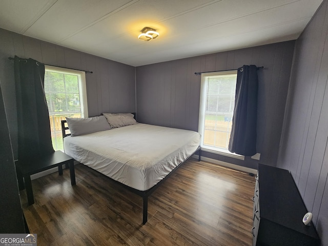 bedroom featuring wood-type flooring, wooden walls, and multiple windows