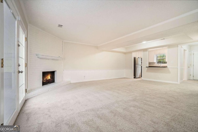 unfurnished living room featuring a textured ceiling, light colored carpet, a brick fireplace, and crown molding