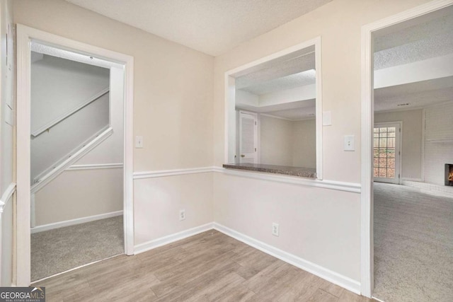 unfurnished room with a brick fireplace, a textured ceiling, and light hardwood / wood-style flooring