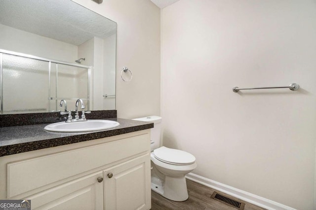 bathroom with vanity, a textured ceiling, hardwood / wood-style floors, toilet, and a shower with shower door