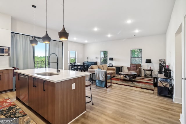 kitchen featuring sink, a kitchen bar, an island with sink, hanging light fixtures, and light wood-type flooring