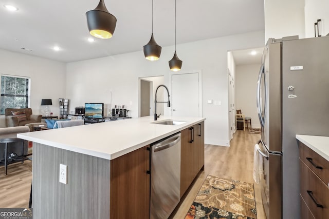 kitchen featuring stainless steel appliances, a center island with sink, sink, pendant lighting, and light wood-type flooring