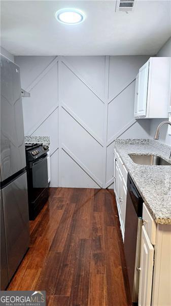 kitchen featuring sink, light stone counters, appliances with stainless steel finishes, dark hardwood / wood-style floors, and white cabinets