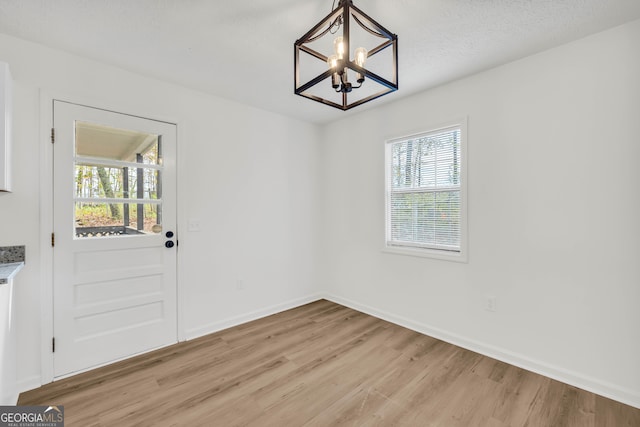 unfurnished dining area with light hardwood / wood-style floors, a chandelier, and a textured ceiling