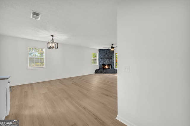 unfurnished living room featuring a stone fireplace, a textured ceiling, light wood-type flooring, and ceiling fan with notable chandelier