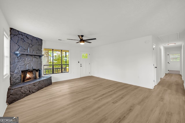 unfurnished living room featuring a stone fireplace, a wealth of natural light, ceiling fan, and light hardwood / wood-style flooring