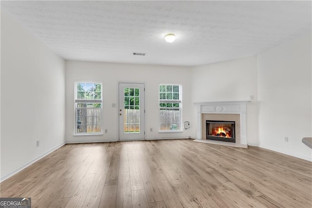 unfurnished living room featuring visible vents, a fireplace, a textured ceiling, and wood finished floors