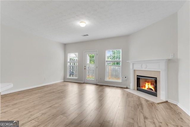 unfurnished living room featuring a textured ceiling, wood finished floors, baseboards, and a premium fireplace