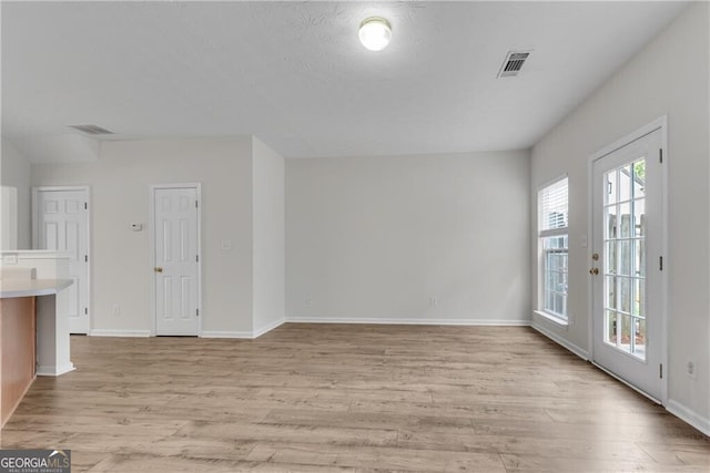 unfurnished living room featuring visible vents, light wood-style flooring, and baseboards