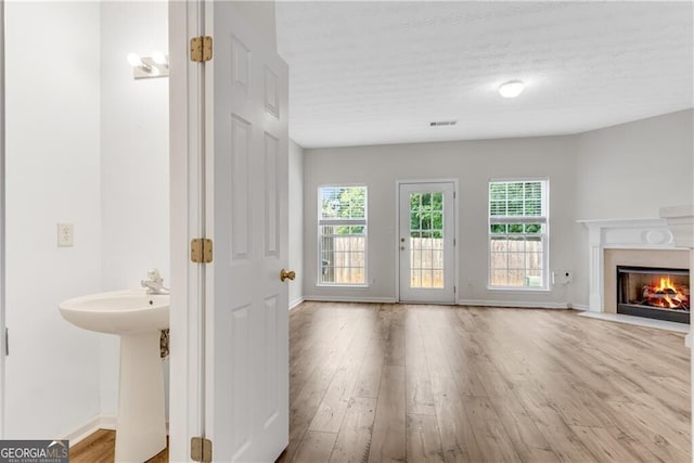 unfurnished living room with a high end fireplace, plenty of natural light, visible vents, and wood finished floors