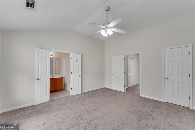 unfurnished bedroom featuring baseboards, visible vents, ensuite bath, vaulted ceiling, and light colored carpet