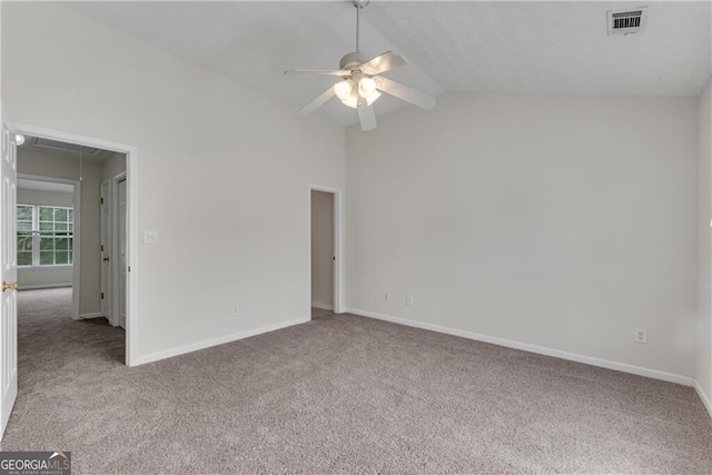 carpeted empty room featuring visible vents, lofted ceiling, baseboards, attic access, and ceiling fan