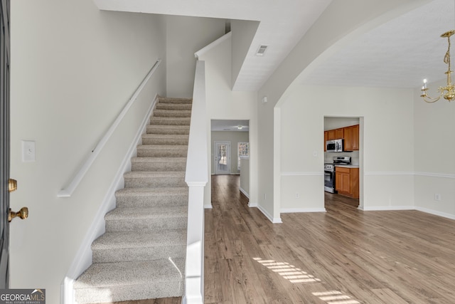 entryway featuring arched walkways, a notable chandelier, visible vents, light wood-style flooring, and stairs