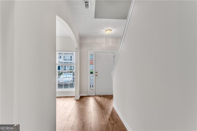 foyer entrance featuring arched walkways, visible vents, baseboards, and wood finished floors