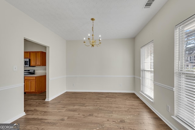 unfurnished dining area featuring baseboards, visible vents, an inviting chandelier, light wood-style flooring, and a textured ceiling