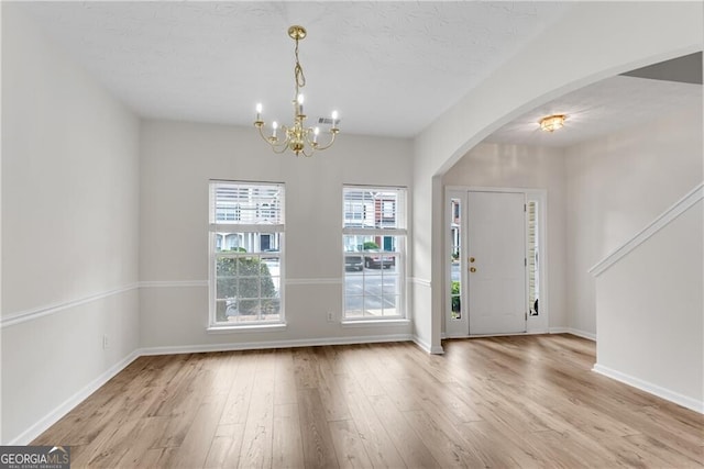 foyer with a textured ceiling, wood finished floors, arched walkways, baseboards, and a chandelier