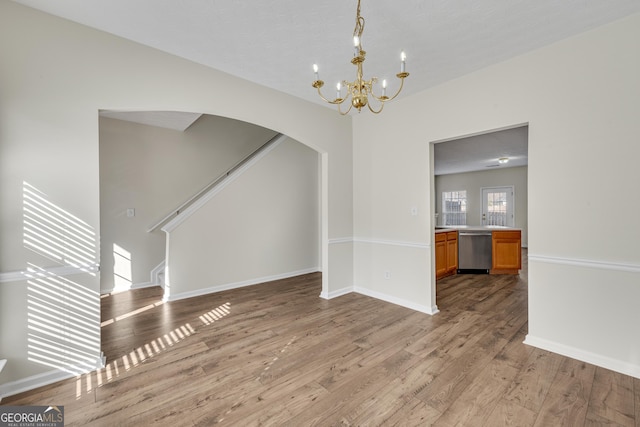 unfurnished dining area featuring baseboards, an inviting chandelier, arched walkways, stairs, and light wood-type flooring