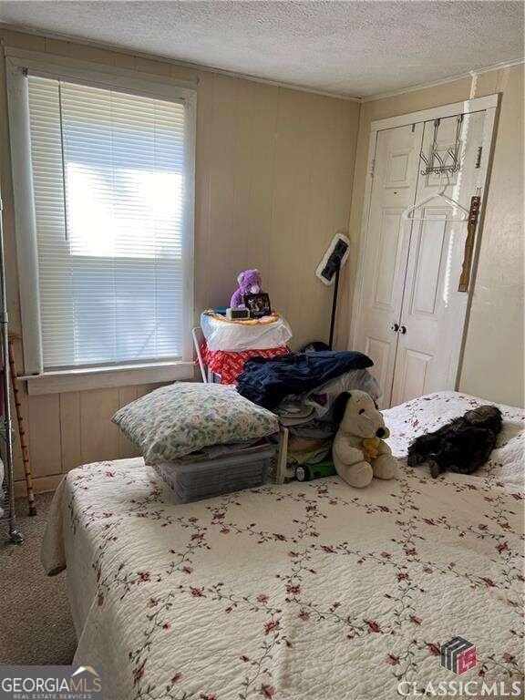 carpeted bedroom featuring wooden walls, a textured ceiling, and a closet