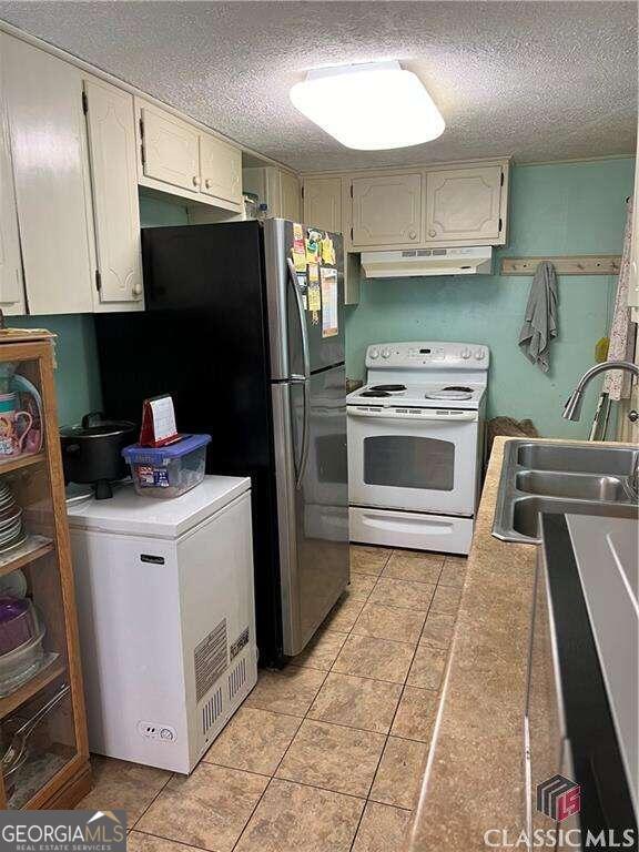 kitchen featuring light tile patterned flooring, white electric range oven, a textured ceiling, fridge, and sink