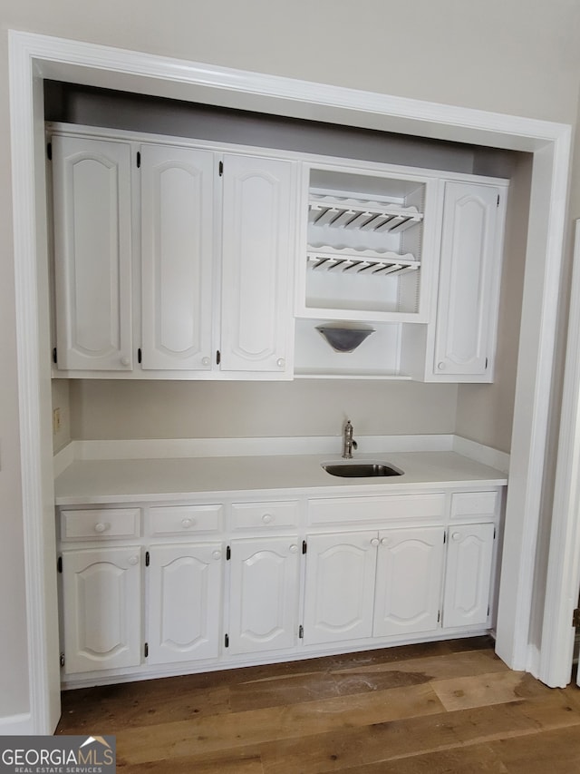 bar with dark wood-type flooring, sink, and white cabinets