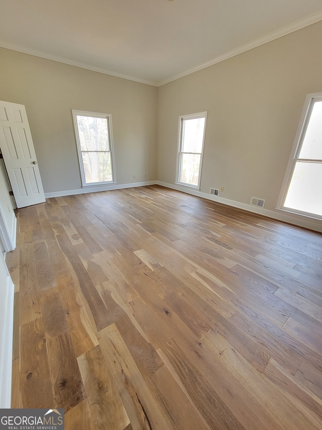 empty room with a healthy amount of sunlight, light wood-type flooring, and ornamental molding