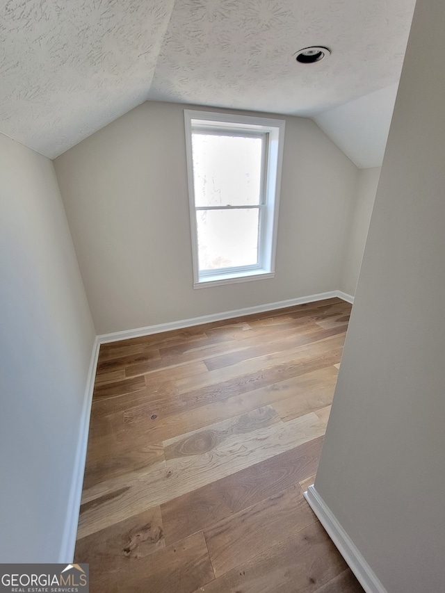 additional living space featuring light hardwood / wood-style floors, a textured ceiling, and vaulted ceiling